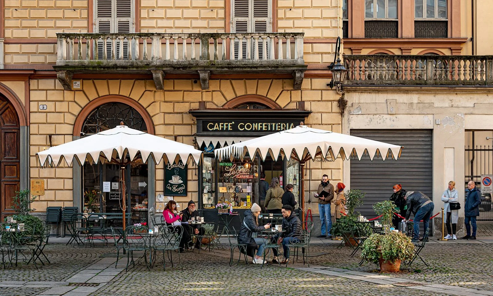 Facciata color ocra del Caffè Al Bicerin in piazza della Consolata, con insegna Caffè Confetteria, ombrelloni bianchi e tavolini all'aperto