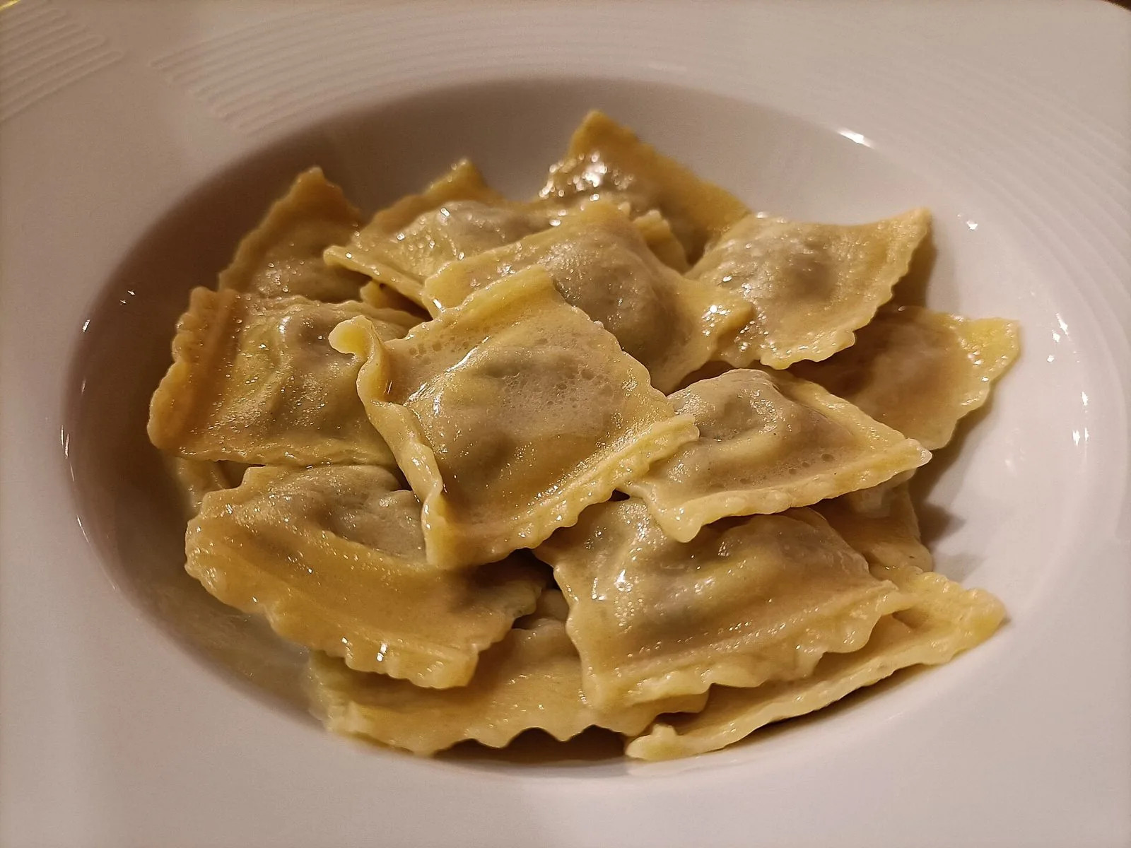 Piatto fondo bianco con agnolotti piemontesi di forma quadrata, conditi con burro