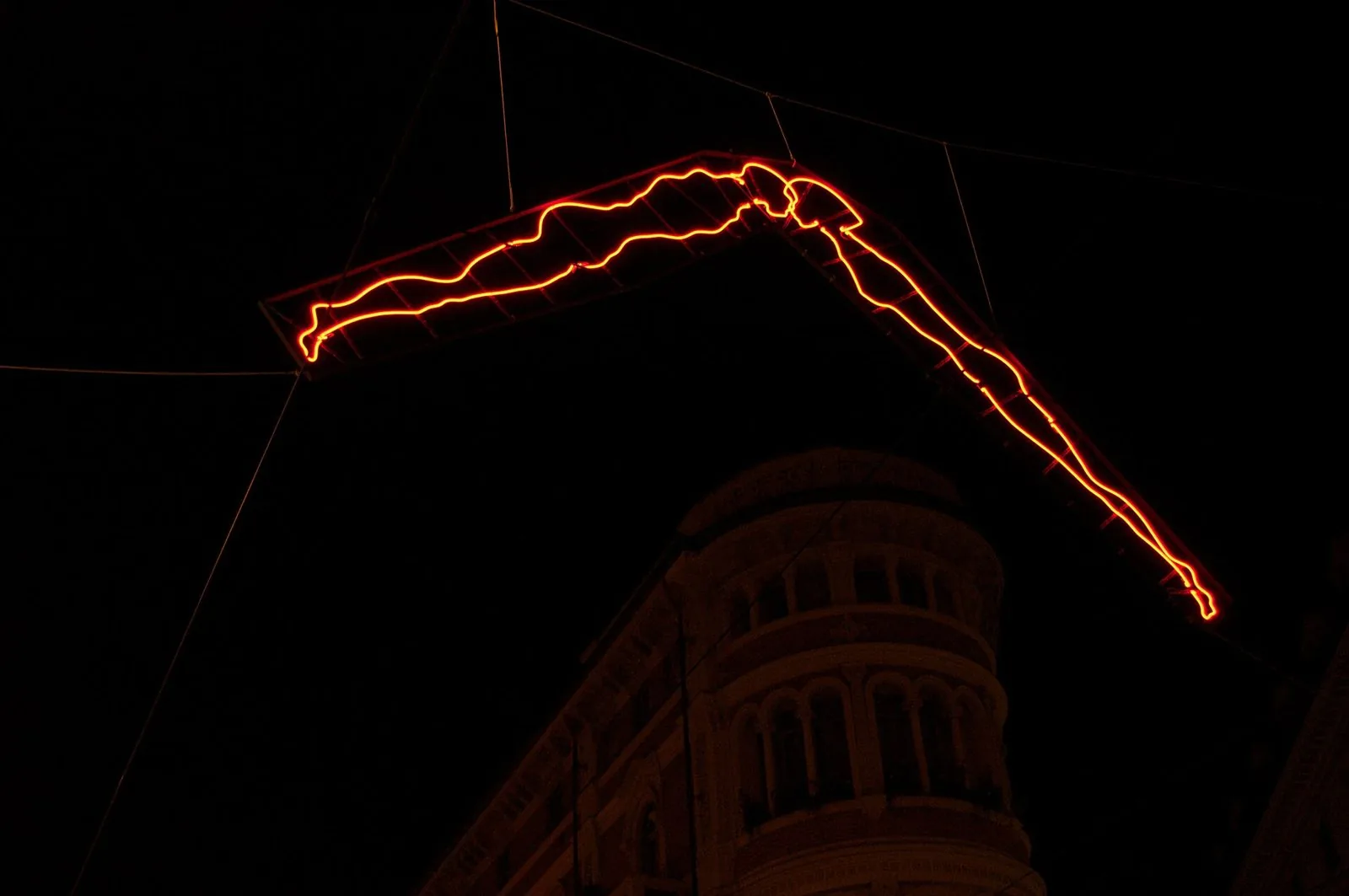 Installazione luminosa al neon rosso a forma di figura umana in volo, sospesa di notte sopra una via del centro di Torino