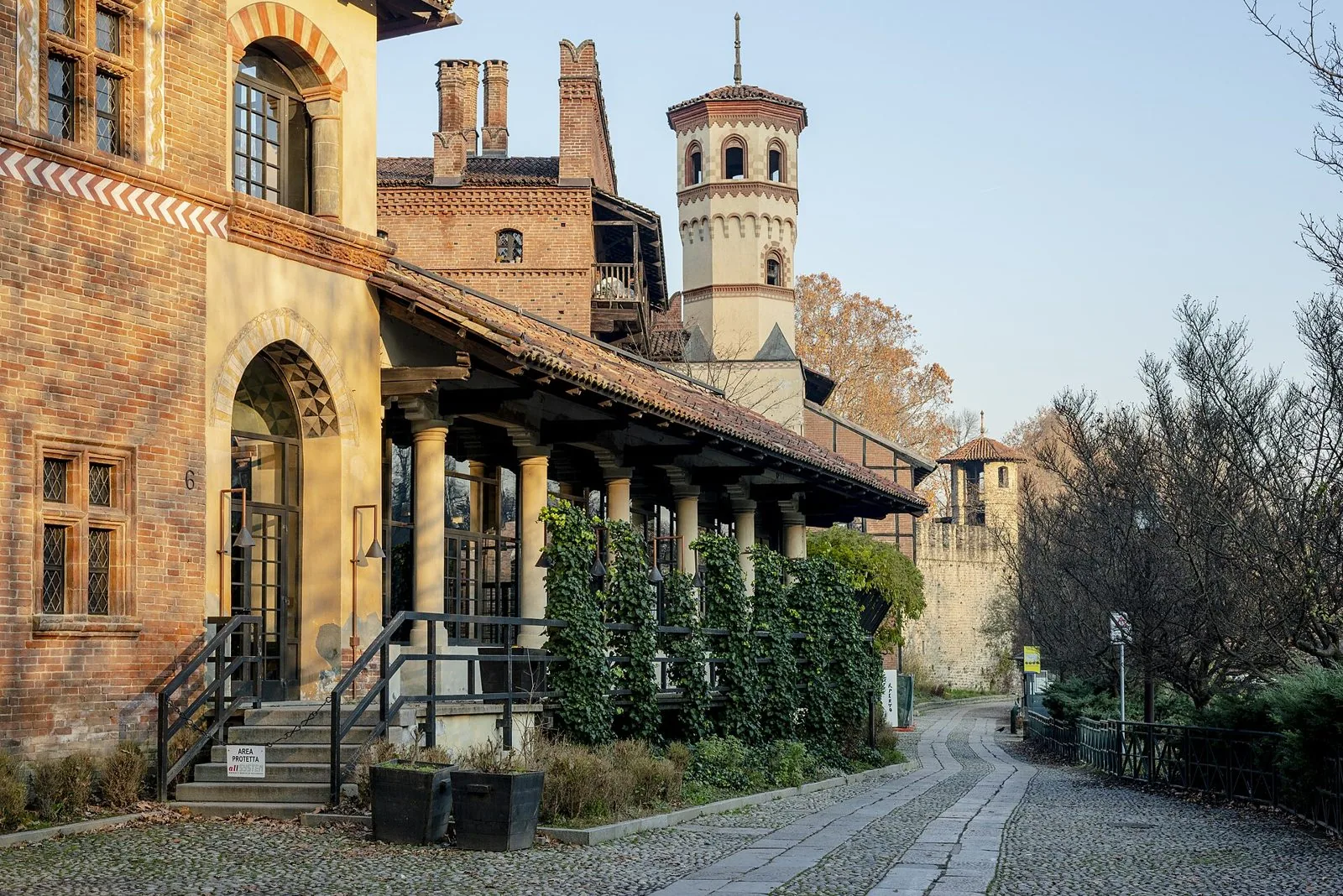 Una via acciottolata del Borgo Medievale al Parco del Valentino, con edifici in mattoni, un porticato coperto d'edera e una torre ottagonale