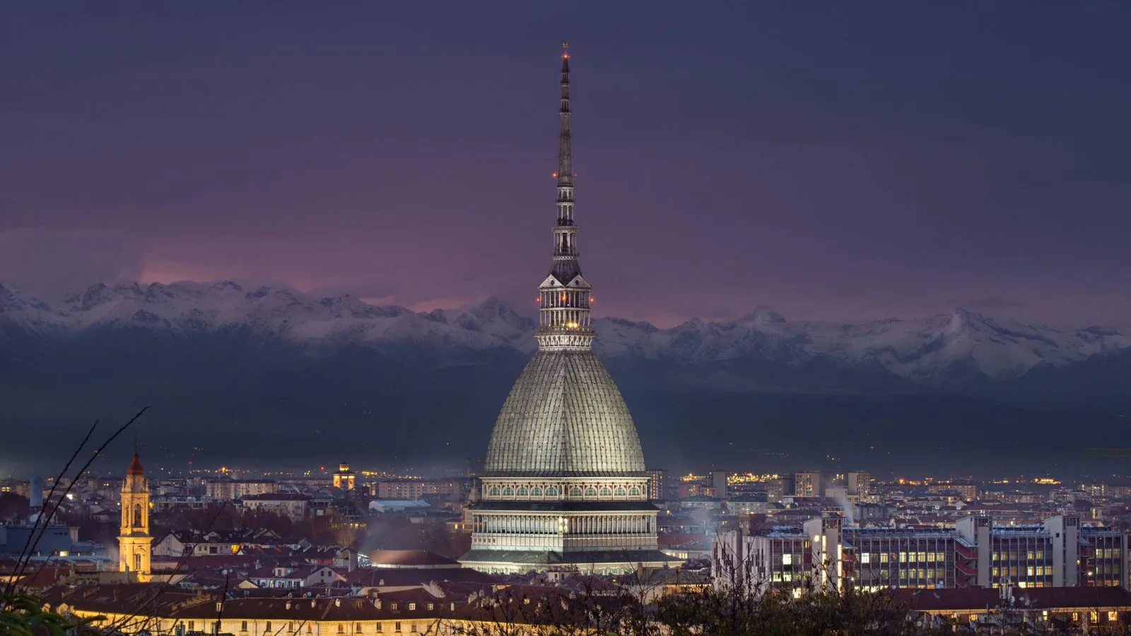 La Mole Antonelliana illuminata di sera sopra i tetti di Torino